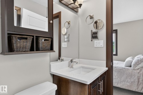 Vanity with a white countertop and integrated sink, complemented by a dark wood-finish cabinet and medicine cabinet with open shelving - 8506 80 Avenue, Edmonton, AB 
