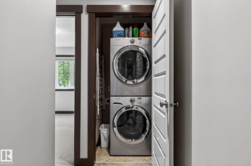 Stacked laundry appliances within a dedicated closet, featuring a white louvered door, dark wood trim, and tile flooring - 8506 80 Avenue, Edmonton, AB 