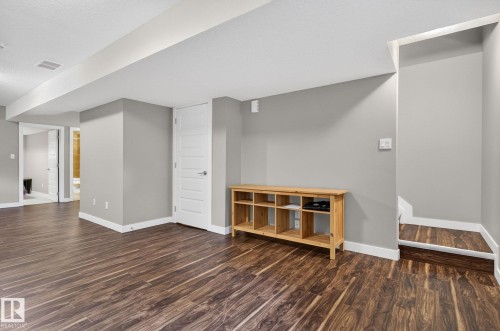Spacious finished area featuring wood-finish flooring, light gray walls, white baseboards, and white paneled doors - 8506 80 Avenue, Edmonton, AB 