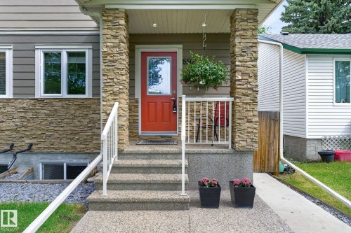 Inviting front entry featuring a red paneled door with glass insert, stacked stone veneer siding, and a covered porch - 8506 80 Avenue, Edmonton, AB 