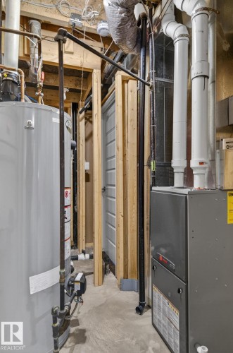 Utility space featuring a water heater, furnace, exposed wood framing, white PVC plumbing, and concrete flooring - 8506 80 Avenue, Edmonton, AB 