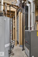 Utility space featuring a water heater, furnace, exposed wood framing, white PVC plumbing, and concrete flooring - 