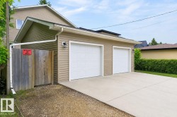 Attached two-car garage with white paneled garage doors, tan horizontal siding, exterior lighting fixture, and concrete driveway - 