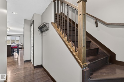 Dark wood-finish staircase featuring a light wood-finish newel post and handrail with black iron balusters - 8506 80 Avenue, Edmonton, AB 