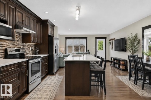 Spacious kitchen featuring dark wood cabinetry, stainless steel appliances, a tile backsplash, and a large island with seating - 8506 80 Avenue, Edmonton, AB 