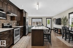 Spacious kitchen featuring dark wood cabinetry, stainless steel appliances, a tile backsplash, and a large island with seating - 
