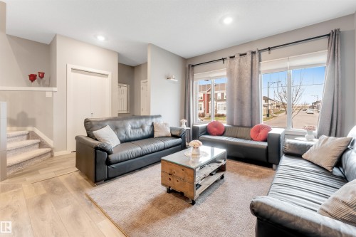 Bright living space featuring large windows with street views, light wood-finish flooring, recessed lighting, and a carpeted staircase - 2652 Maple Way, Edmonton, AB - Indoor Photo Showing Living Room