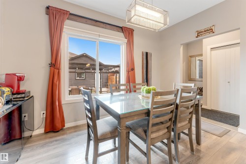 Dining area featuring wood-finish flooring, a contemporary rectangular light fixture, and a large window with exterior property structures - 2652 Maple Way, Edmonton, AB - Indoor Photo Showing Dining Room