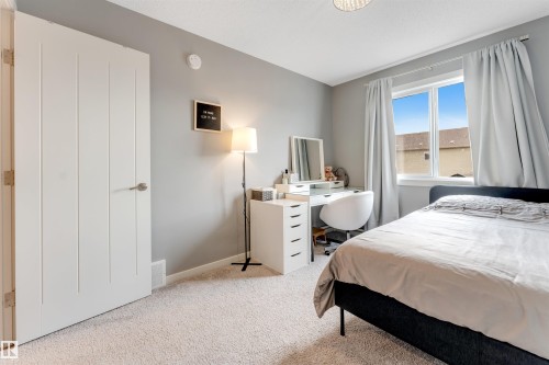 Carpeted bedroom featuring a large window, a modern door with vertical paneling, light gray walls, and a ceiling-mounted light fixture - 2652 Maple Way, Edmonton, AB - Indoor Photo Showing Bedroom
