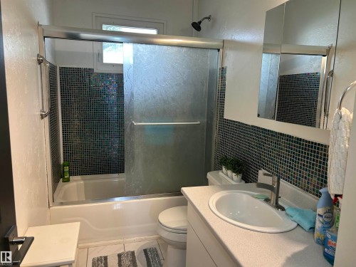 Bathroom with a white bathtub and shower featuring a sliding glass enclosure - 10924 30 Street, Edmonton, AB 