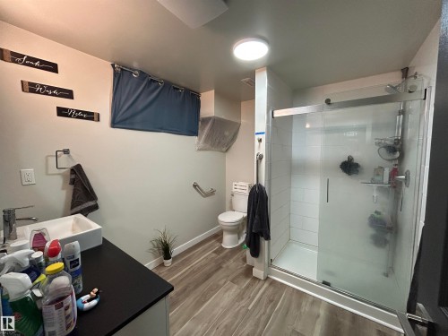 Modern bathroom featuring a glass-enclosed shower with white subway tile, a vessel sink on a dark countertop, wood-finish flooring, and a round overhead light fixture - 10924 30 Street, Edmonton, AB 