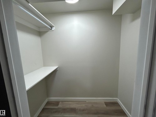 Spacious walk-in closet featuring light grey walls, wood-finish flooring, a white clothes rod, and a white storage shelf - 10924 30 Street, Edmonton, AB 