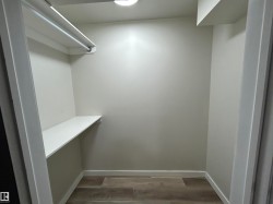 Spacious walk-in closet featuring light grey walls, wood-finish flooring, a white clothes rod, and a white storage shelf - 