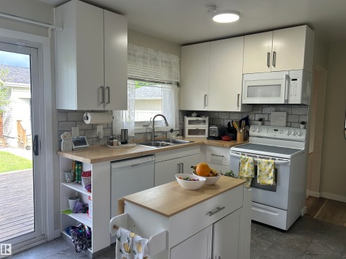 Kitchen featuring white cabinetry, light wood-finish countertops, subway tile backsplash, and dark tile flooring - 10924 30 Street, Edmonton, AB 