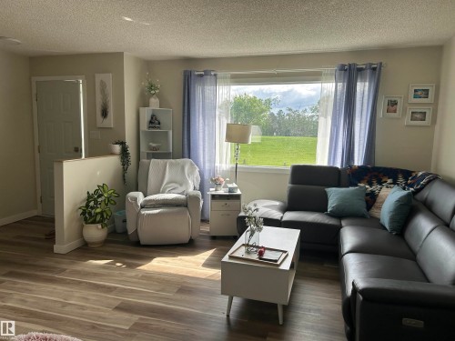 Spacious living area featuring wood-finish flooring, a large picture window, light neutral wall tones, a partial wall partition, and a solid white interior door - 10924 30 Street, Edmonton, AB 