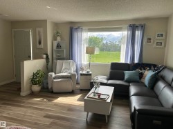 Spacious living area featuring wood-finish flooring, a large picture window, light neutral wall tones, a partial wall partition, and a solid white interior door - 