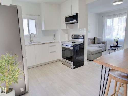 Modern kitchen featuring a stainless steel refrigerator, white cabinetry, integrated sink, electric range, and wood-finish flooring - 9909 157 Street, Edmonton, AB 