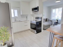 Modern kitchen featuring a stainless steel refrigerator, white cabinetry, integrated sink, electric range, and wood-finish flooring - 