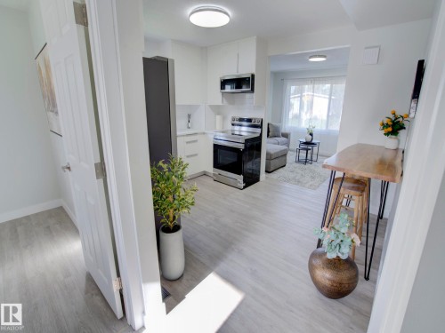 Open-concept kitchen featuring white cabinetry, stainless steel appliances, and light wood-finish flooring - 9909 157 Street, Edmonton, AB 
