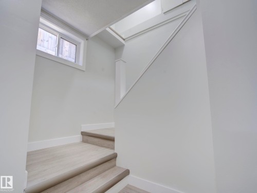 Stairwell featuring light-toned wood-finish flooring, white painted walls, white baseboards, and a contemporary window with natural light - 9909 157 Street, Edmonton, AB 
