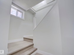 Stairwell featuring light-toned wood-finish flooring, white painted walls, white baseboards, and a contemporary window with natural light - 