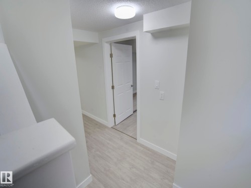 Hallway featuring light-toned wood-finish flooring, white baseboards, and a flush-mount ceiling light fixture - 9909 157 Street, Edmonton, AB 