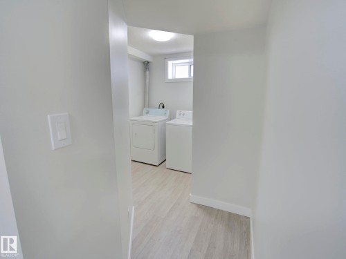 Dedicated laundry area featuring a washer and dryer, light wood-finish flooring, a functional window, and overhead lighting - 9909 157 Street, Edmonton, AB 