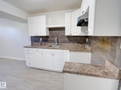 Kitchenette featuring white cabinetry, a stainless steel sink, patterned countertops, and a complementary backsplash - 