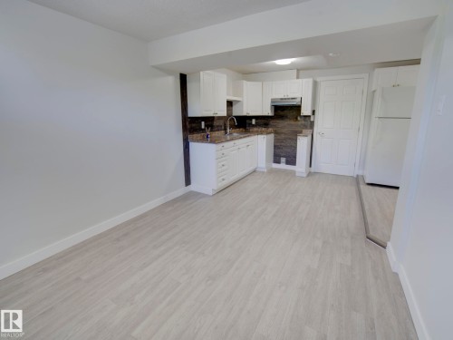 Kitchenette featuring white cabinetry, stone-finish countertops, tile backsplash, and light wood-finish flooring - 9909 157 Street, Edmonton, AB 