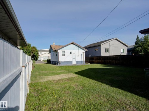 Spacious backyard featuring a large grass area, a partial white privacy fence, and a dark wood privacy fence - 9909 157 Street, Edmonton, AB 