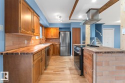 Kitchen featuring wood-finish cabinetry, wood-finish countertops, stainless steel appliances, brick-style backsplash, and wood-finish flooring - 