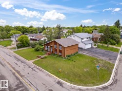 Corner lot property featuring a brown siding exterior with white trim, a gabled roof, and a mature treed setting - 