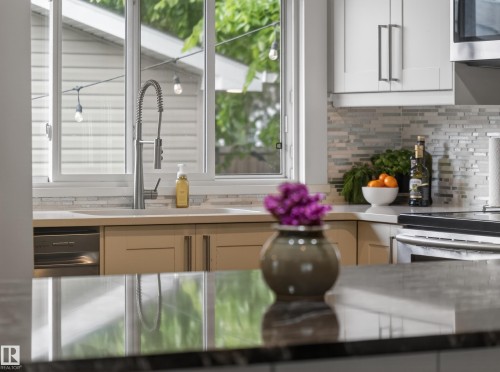 Modern kitchen featuring a stainless steel pull-down faucet, light-toned cabinetry, light-colored countertops, a mosaic tile backsplash, and stainless steel appliances - 15803 83 Avenue, Edmonton, AB 