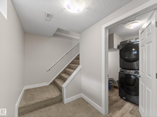 Laundry area featuring stacked appliances, wood-finish flooring, and an overhead light fixture - 15803 83 Avenue, Edmonton, AB 