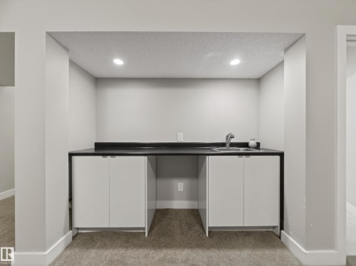 Wet bar area featuring a dark countertop, stainless steel sink with a chrome faucet, and white base cabinets - 15803 83 Avenue, Edmonton, AB 