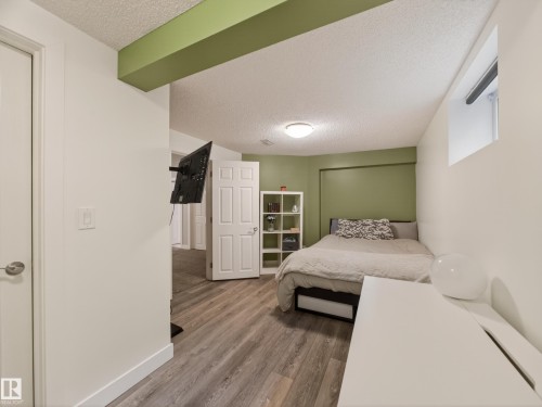 Room featuring wood-finish flooring, a neutral color palette with an accent wall, a built-in wall-mounted television bracket, a window, and a ceiling light fixture - 15803 83 Avenue, Edmonton, AB 