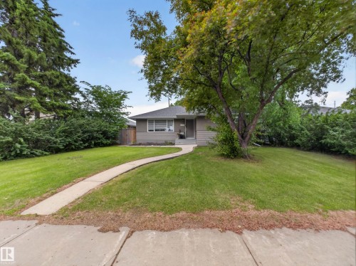 Exterior featuring a light gray facade, a gabled roof, and a mature front yard tree - 15803 83 Avenue, Edmonton, AB 