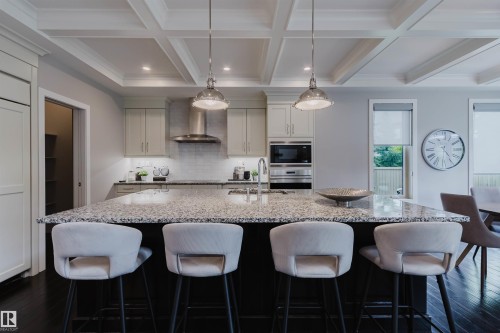 Kitchen featuring a large island with stone countertops, a stainless steel range hood, built-in microwave, integrated refrigerator, and dark wood-finish flooring - 3435 Keswick Boulevard, Edmonton, AB 