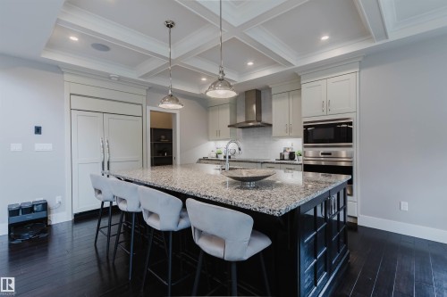 Gourmet kitchen featuring a large island with a stone countertop, built-in stainless steel appliances, light-toned cabinetry, dark wood-finish flooring, and a coffered ceiling - 3435 Keswick Boulevard, Edmonton, AB 