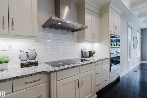 Kitchen featuring light-toned cabinetry, granite-style countertops, an integrated cooktop, a stainless steel range hood, and built-in stainless steel appliances - 3435 Keswick Boulevard, Edmonton, AB 