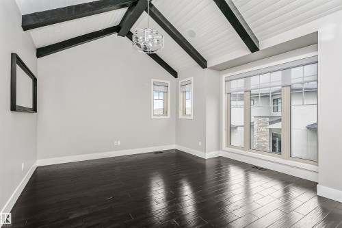 Vaulted ceiling with exposed black beams and white wood-finish planks, dark wood-finish flooring, large multi-pane windows, modern spherical chandelier, and a smaller rectangular window - 3435 Keswick Boulevard, Edmonton, AB 