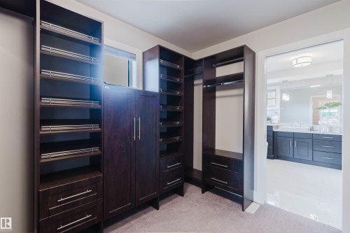 Custom closet system featuring dark wood-finish cabinetry, integrated shelving, multiple hanging rods, and sleek drawer pulls - 3435 Keswick Boulevard, Edmonton, AB 