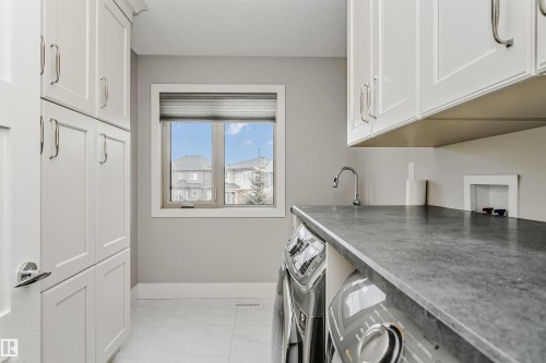 Utility room featuring extensive white shaker cabinetry, dark stone-finish countertop, and a window with natural light - 3435 Keswick Boulevard, Edmonton, AB 