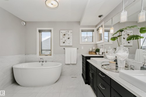 Freestanding soaking tub with chrome fixtures, dual vessel sinks, black cabinetry with chrome hardware, white countertops, and expansive mirror - 3435 Keswick Boulevard, Edmonton, AB 
