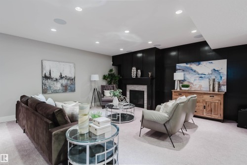 Spacious living area featuring light-toned carpeting, recessed ceiling lighting, and a prominent fireplace with a light-colored tile surround and dark mantelpiece - 3435 Keswick Boulevard, Edmonton, AB 