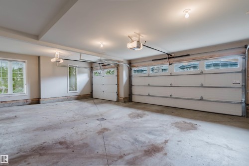 Spacious garage featuring two overhead doors with window panels, an additional single overhead door with window panels, multiple windows providing natural light, and ceiling-mounted garage door openers - 3435 Keswick Boulevard, Edmonton, AB 