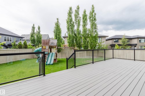 Expansive backyard featuring a new composite deck, black metal and glass panel railing, a green lawn, and a wood privacy fence - 3435 Keswick Boulevard, Edmonton, AB 