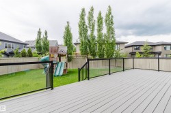 Expansive backyard featuring a new composite deck, black metal and glass panel railing, a green lawn, and a wood privacy fence - 