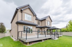 Expansive rear exterior featuring a multi-level deck with glass panel railings, a built-in gazebo, and a manicured lawn - 