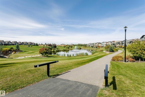 Paved walking path alongside a water feature with a fountain, surrounded by manicured green spaces and residential properties - 3435 Keswick Boulevard, Edmonton, AB 